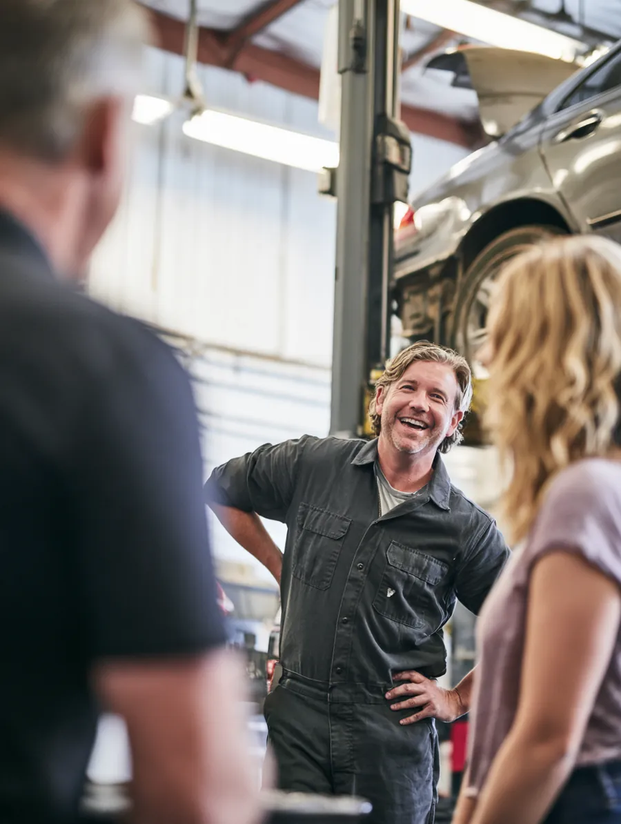 Mechanic in his 40s with car owner in her 20s lowering a sedan on the lift while she waits nearby